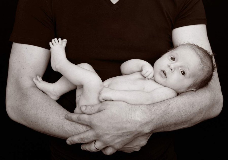 Professional portrait photo of a newborn baby being cradled in Father's arms in a family photography studio Dublin black background
