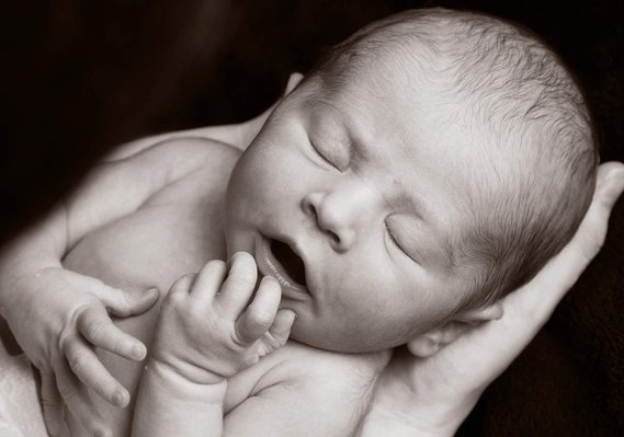 Professional portrait photo of a newborn baby being cradled in Father's hands in a family photography studio Dublin black background 