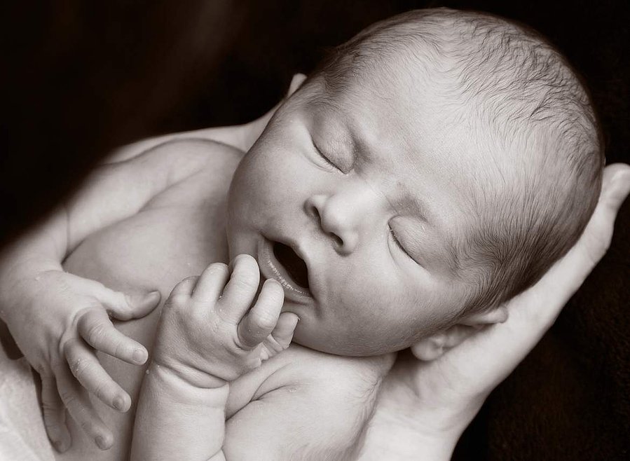 Professional portrait photo of a newborn baby being cradled in Father's hands in a family photography studio Dublin black background
