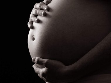 Maternity photo in professional photography studio with black background close up of pregnant bump with mother's hands placed on the bump 