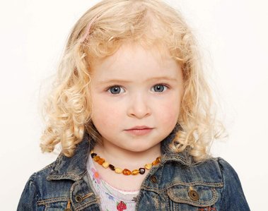 Headshot of young girl with blonde curls and colourful necklaces in professional family portrait studio