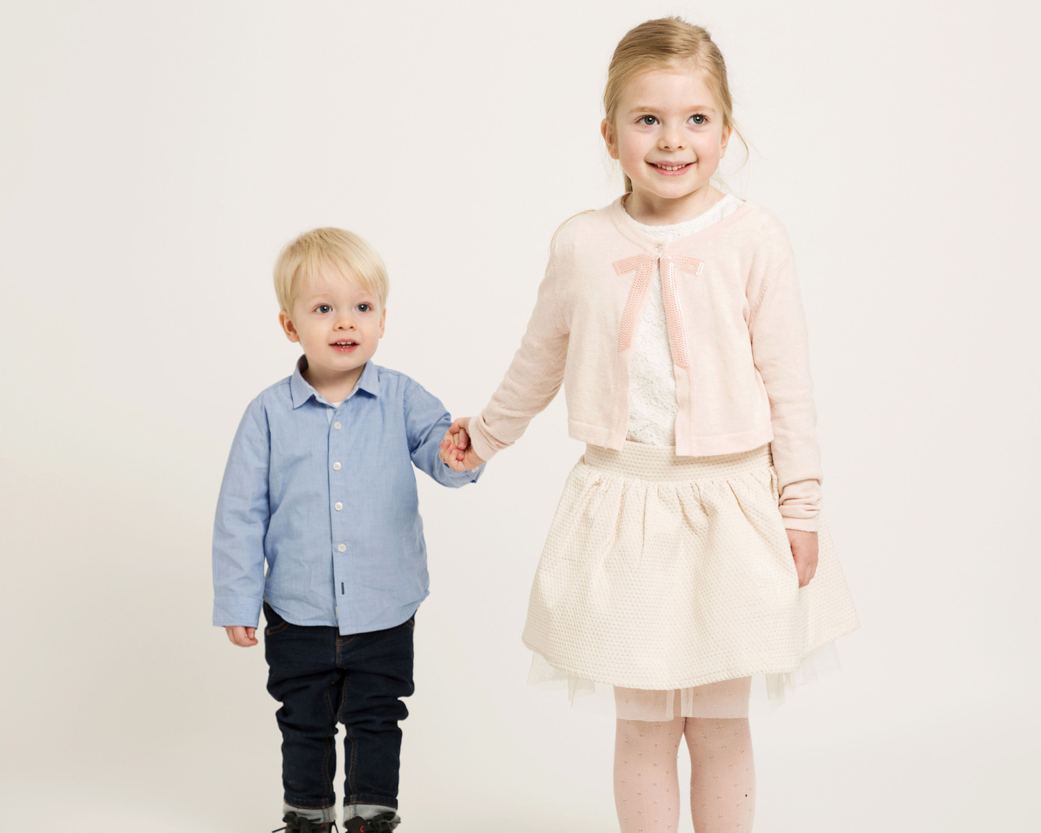 Professional studio portrait of young children, brother and sister holding hands in family photography studio 