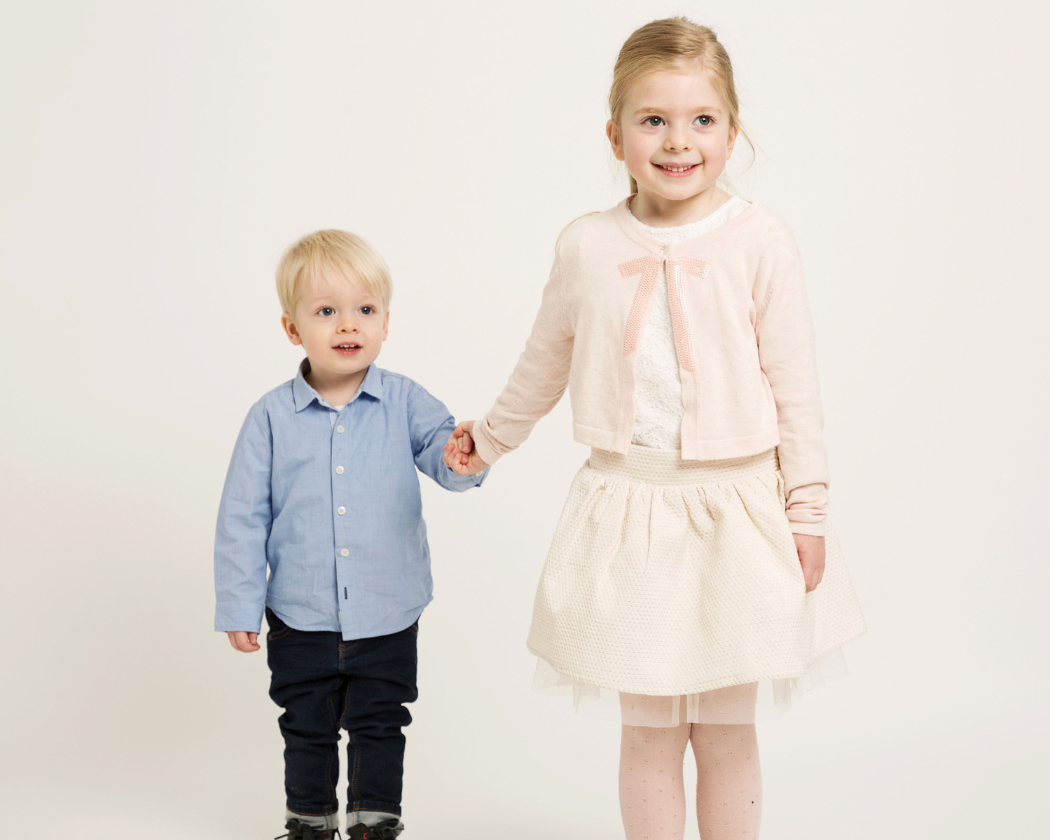 Professional studio portrait of young children, brother and sister holding hands in family photography studio 