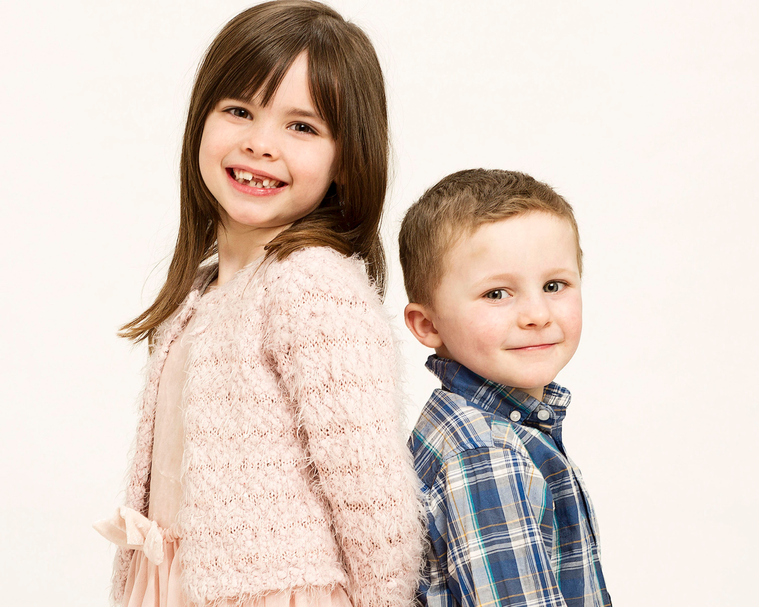 Family photo of sister and brother smiling standing back to back in a professional photography studio in Dublin 