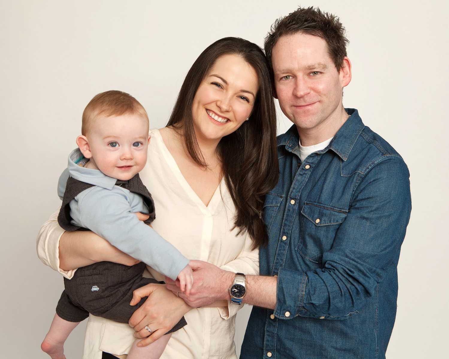 Family portrait of Mom, Dad and young baby in professional photo studio in Dublin white background 