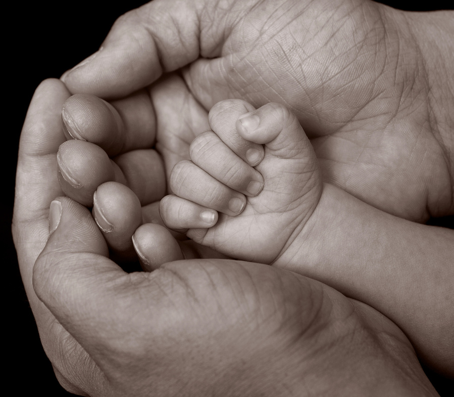 Professional portrait photo of a newborn baby's hand being cradled in Father's hands in a family photography studio Dublin black background