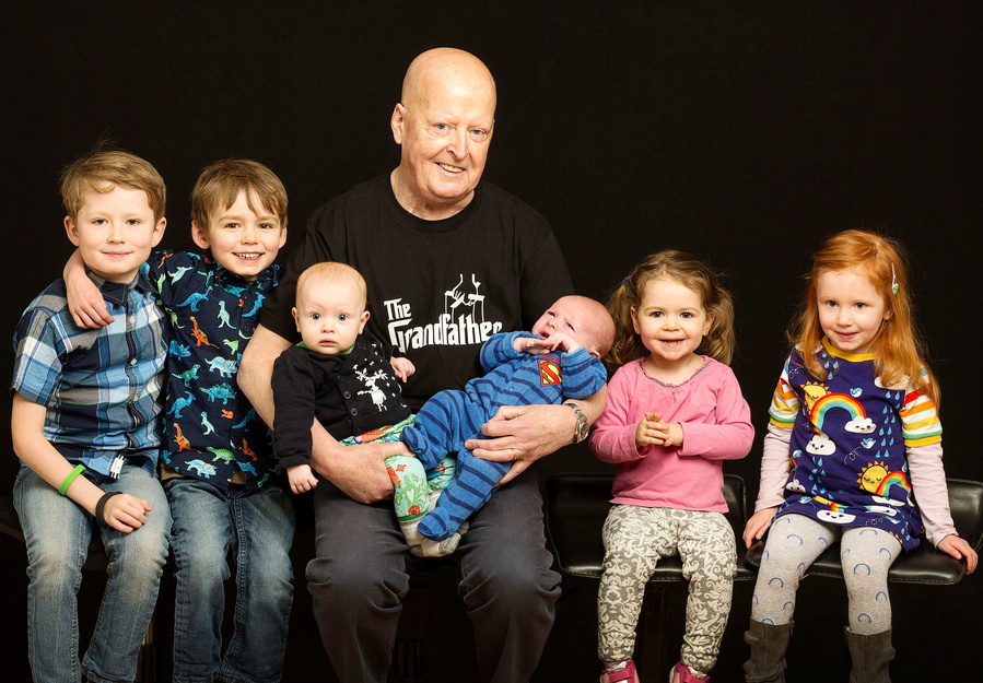 A generational portrait of a grandfather and his grandchildren. Taken in a professional family portrait photography studio in Dublin with a black background