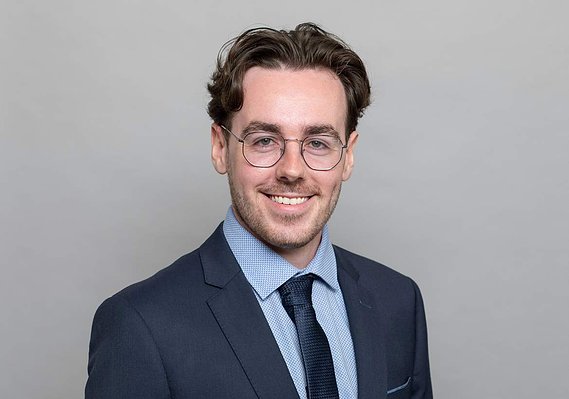 Professional business H&S headshot of young male wearing blue jacket in Dublin corporate photography studio with plain grey background 
