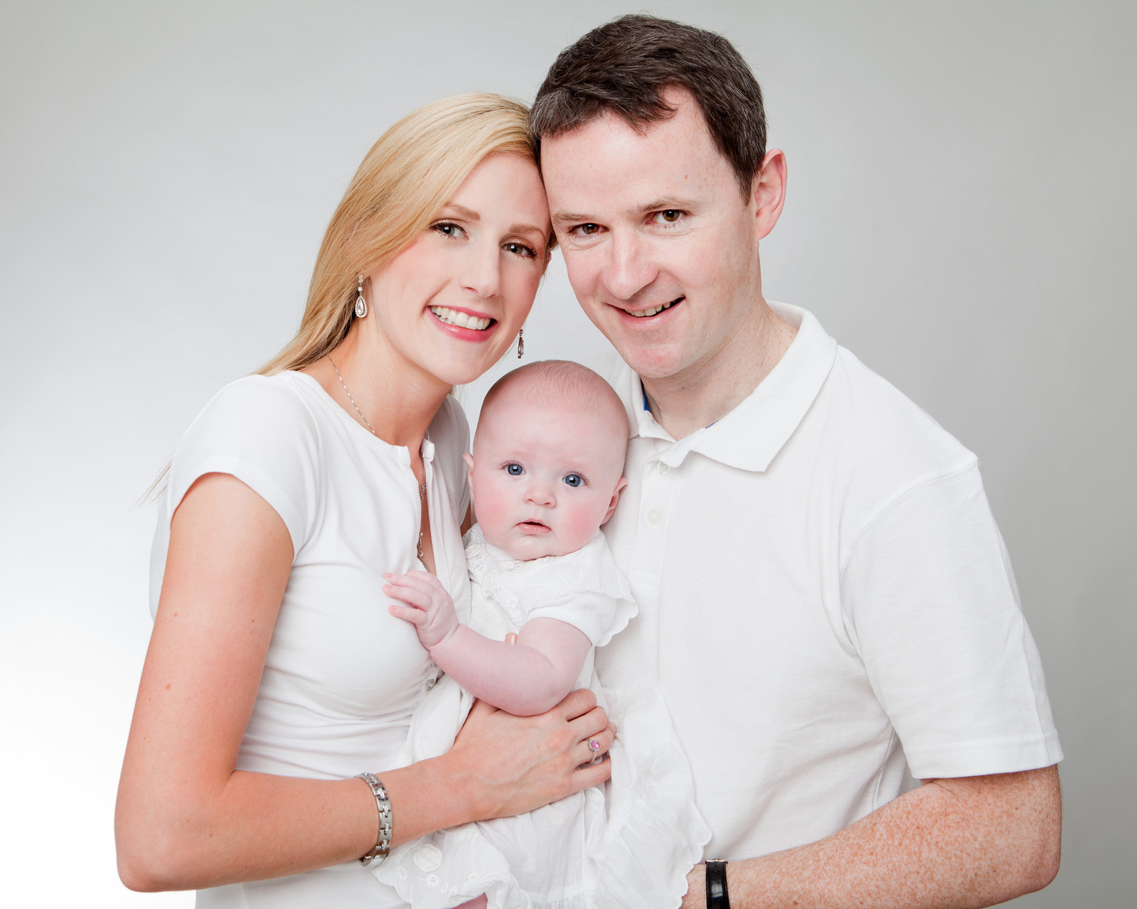 Family portrait of Mom, Dad and young baby in professional photo studio in Dublin white background