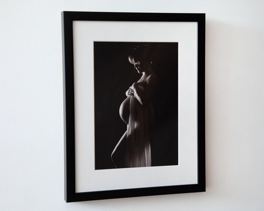 Framed Natural  maternity portrait photo in professional photography studio using black background, side view of pregnant woman bump with draping fabric 