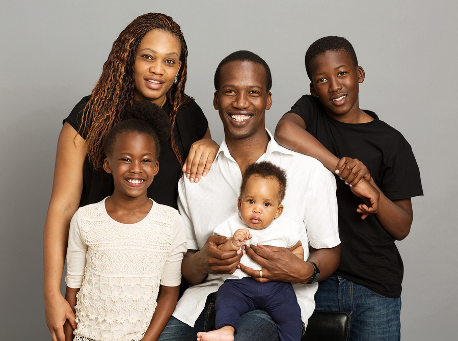 Family portrait of Mother, Father, and three children wearing white and black shirts. Taken in a professional photography studio with grey background