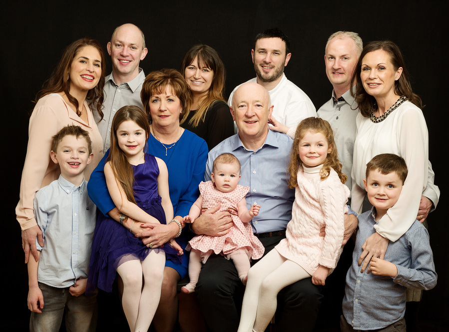 Large group family generational Portrait of a Grandmother and Grandfather with their children and grandchildren photographed in a professional family portrait studio in Dublin black background