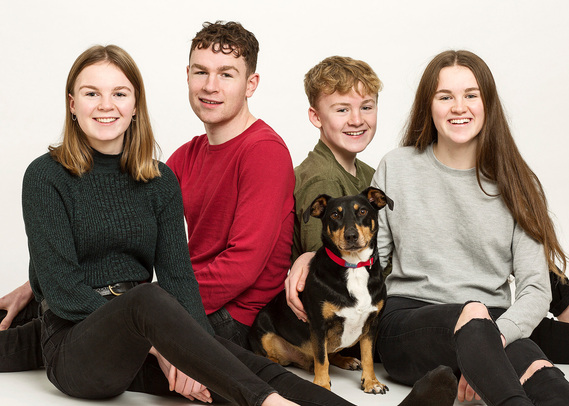 Studio portrait of four teenage brothers and sisters with their family dog in a professional pet photography studio