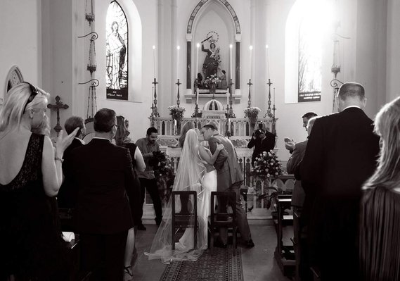 Professional wedding photo of bride and groom kissing at traditional church wedding with congregation clapping wedding photographer Dublin