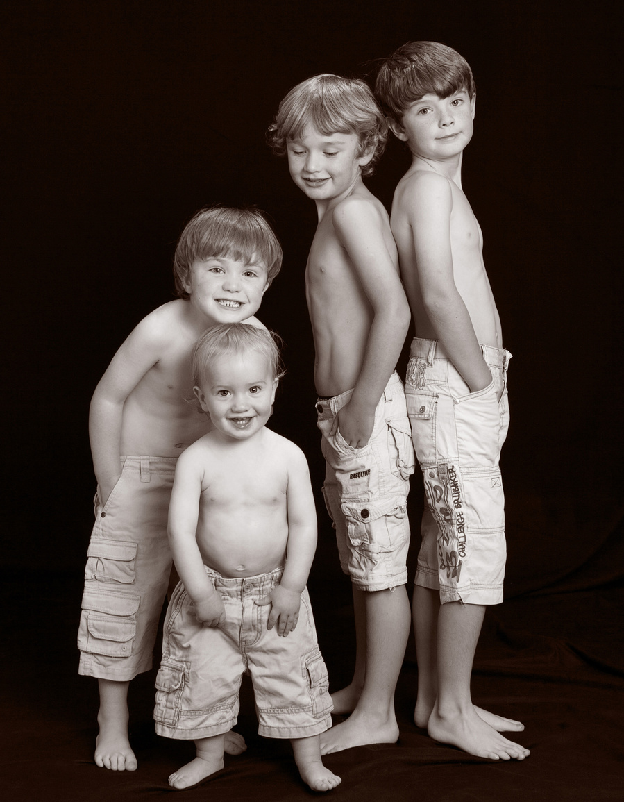 Classic black and white portrait of four young brothers wearing shorts taken in a professional family portrait photography studio 
