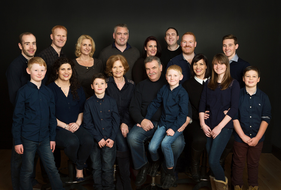 Large group family generational Portrait of a Grandmother and Grandfather with their children and grandchildren all wearing black photographed in a professional family portrait studio in Dublin black background