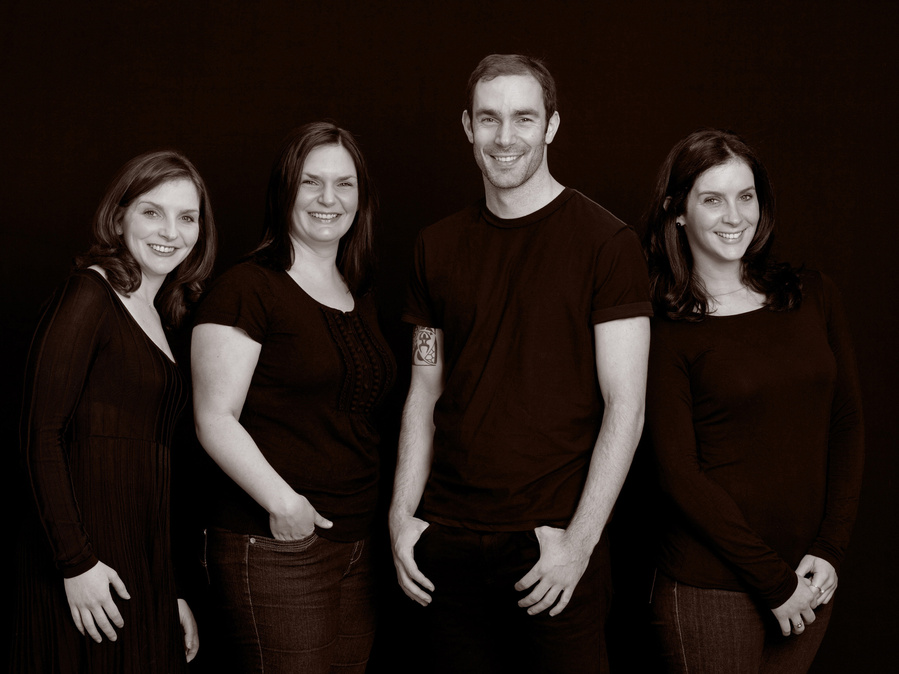 Classic black and white portrait of four adult siblings in professional family photography studio black background