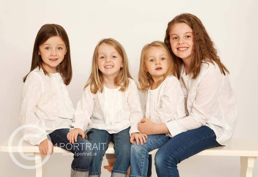 Classic Family portrait of four sisters young children wearing white and denim in a professional photography studio in Dublin white background