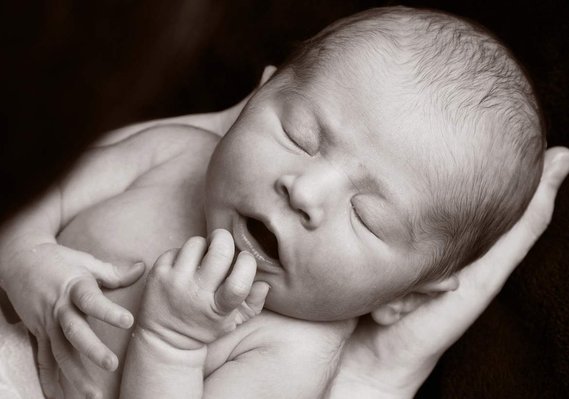 Professional portrait photo of a newborn baby being cradled in Father's hands in a family photography studio Dublin black background 