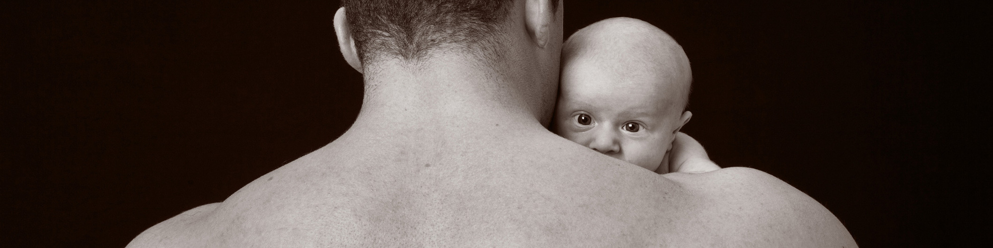 Professional black and white portrait of a tiny newborn baby being held by body builder father in a family photo studio in Dublin  with black background