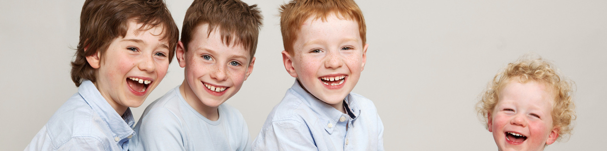 Fun lively family portrait of four brothers in blue shirts sitting on wooden bench in photography studio