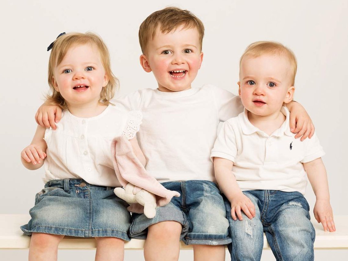 Professional Photography Studio Portrait of Young children, brothers and sister laughing wearing white t shirts and denim