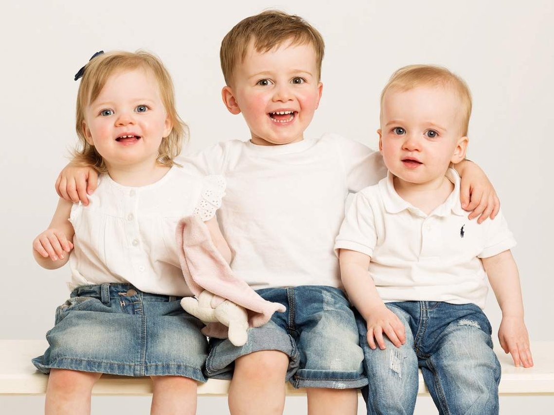 Professional Photography Studio Portrait of Young children, brothers and sister laughing wearing white t shirts and jeans