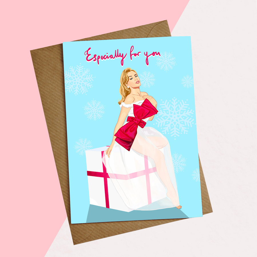 Kylie Minogue Christmas Card by Ryan Hodge illustration.  Sitting on big white present with red ribbon and big bow. Christmas fairy, snow flakes on blue background. Especially for you. Environmentally friendly recycled paper envelope. 