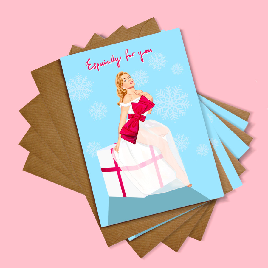 Pack of 4 Kylie Minogue Christmas Card by Ryan Hodge illustration.  Sitting on big white present with red ribbon and big bow. Christmas fairy, snow flakes on blue background. Especially for you. Environmentally friendly recycled paper envelope. 