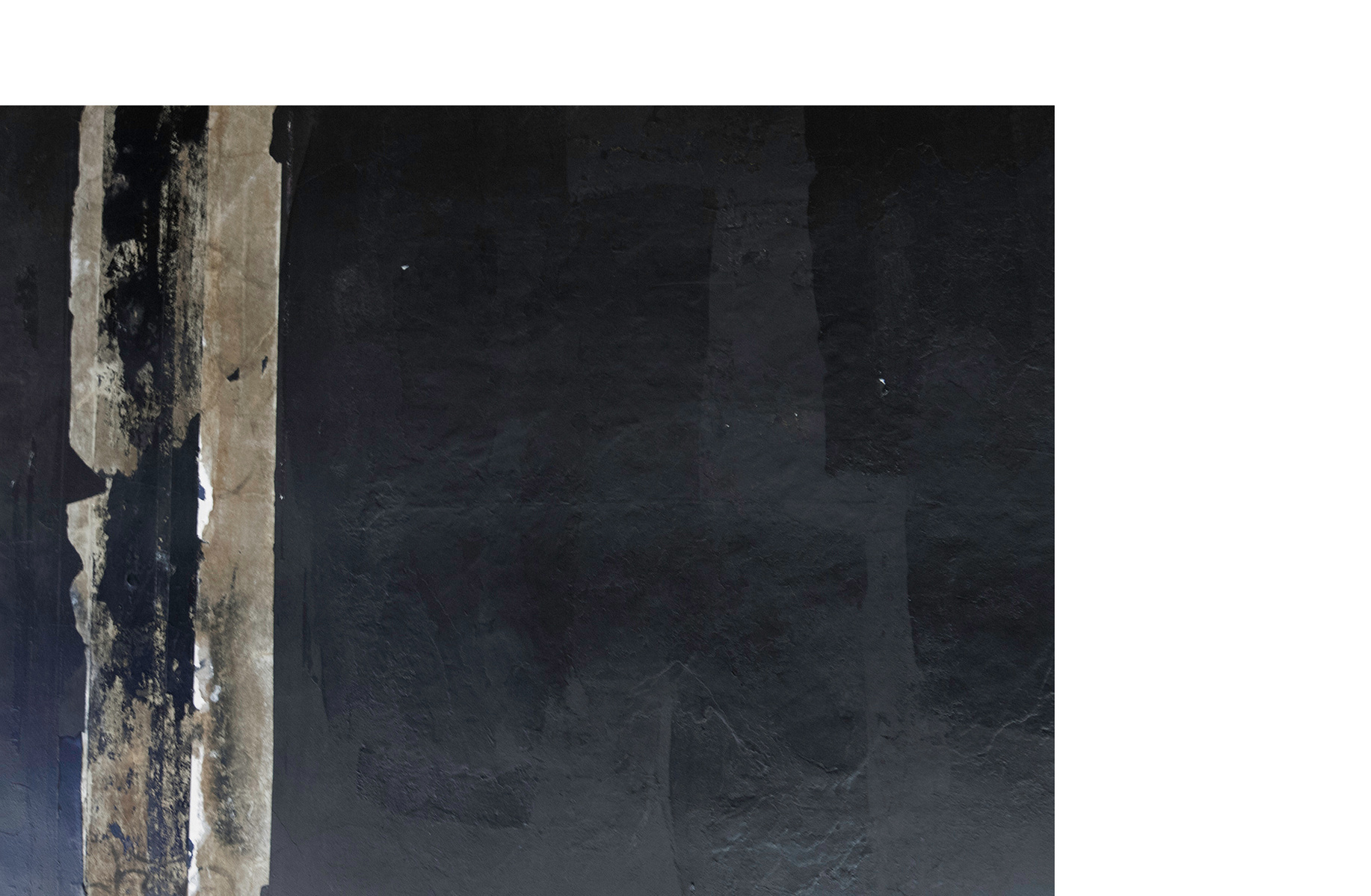 Photograph of black wall with white peeling drywall tape.