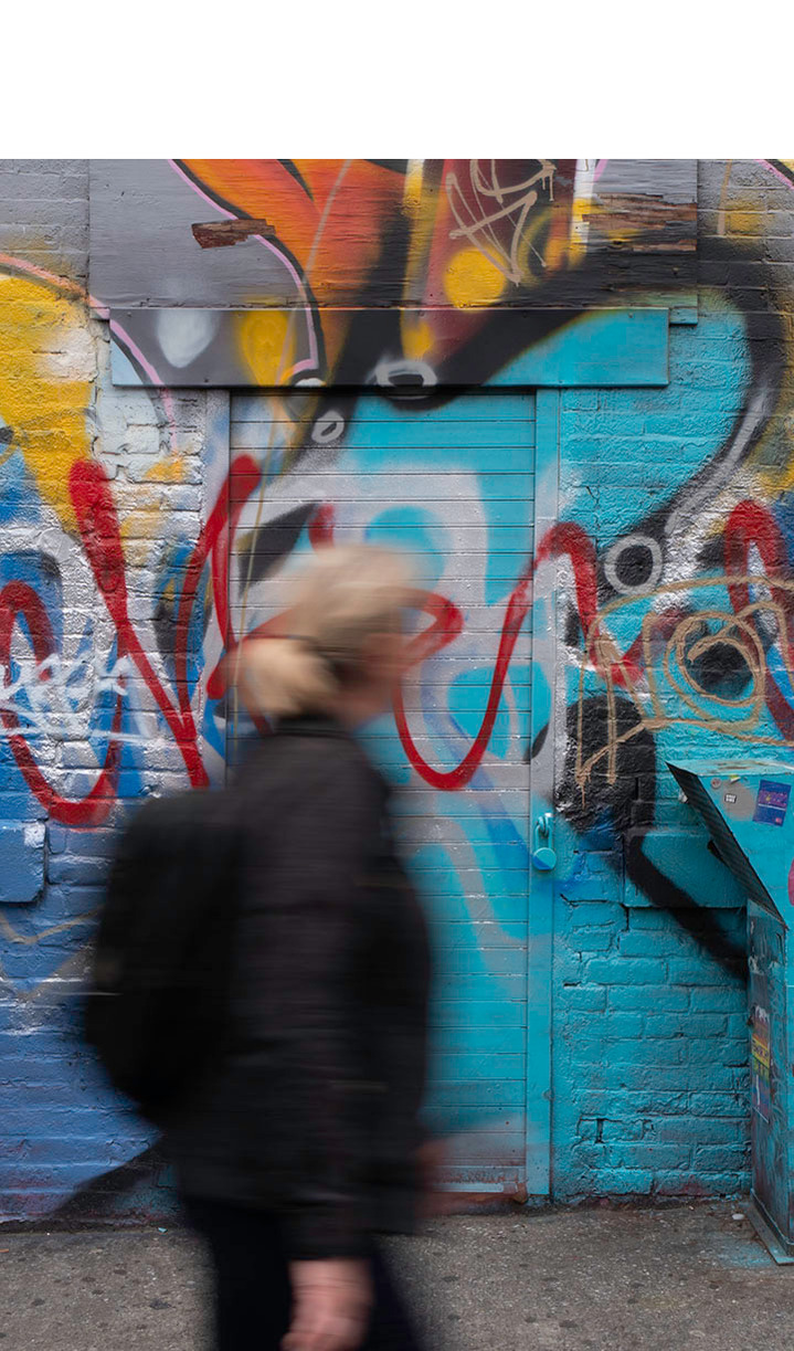 A woman passing an entrance that is located on a wall covered with colourful graffiti