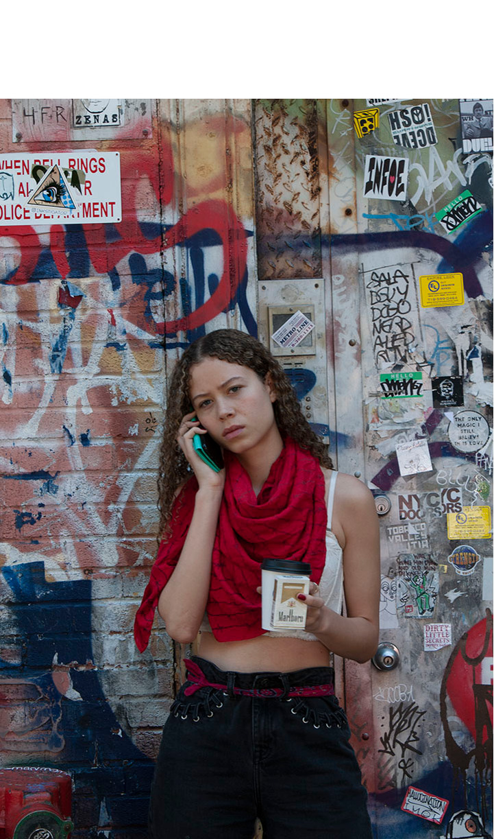 A woman talking on a cell phone while stopped in front of an entrance that is covered with colourful graffiti.