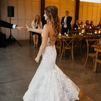 The bride with soft wavy wedding hairstyle holding groom's hand on the dance floor.
