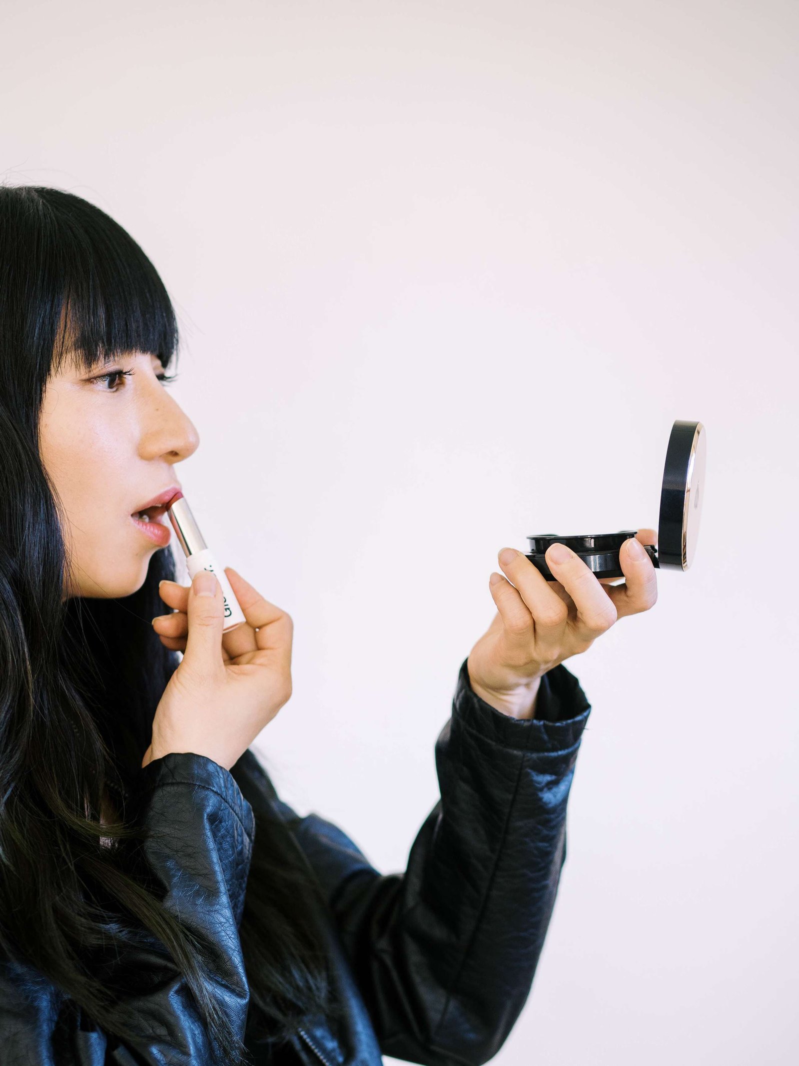 Asian woman looking at mirror applying lipstick