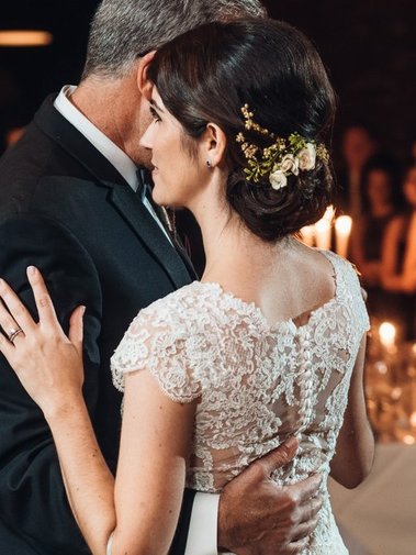 Bride with classic updo chignon and hair accessories dancing with her dad. Wearing lace back wedding dress.