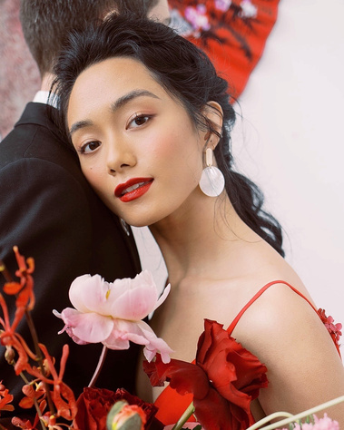 Asian bride wearing red lipstick, holding a big floral bouquet. Asian themed wedding style.