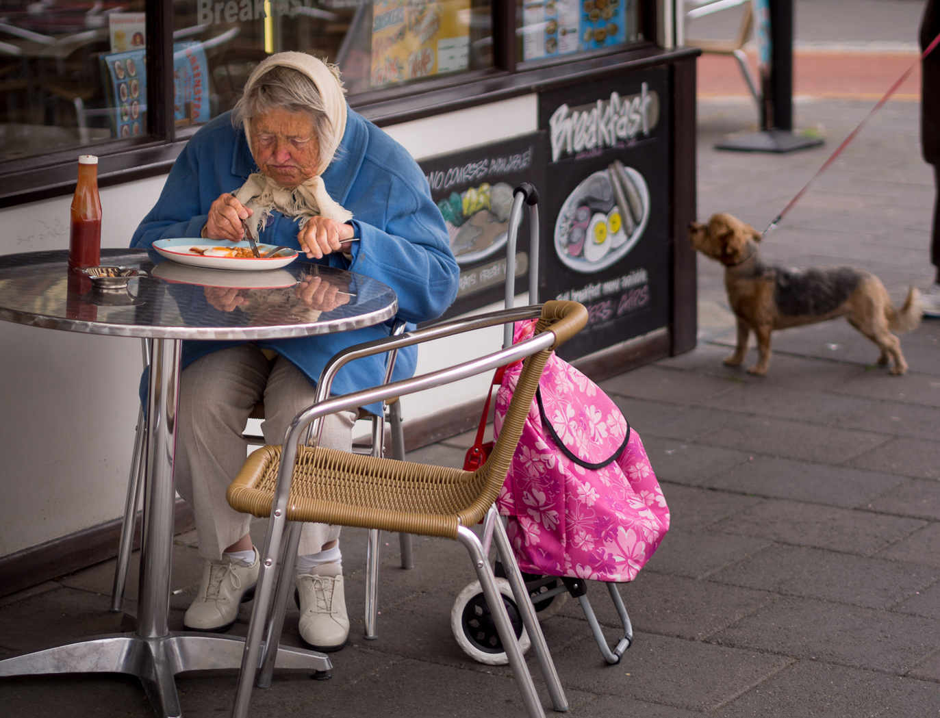 Old lady eating breakfast outdoors.