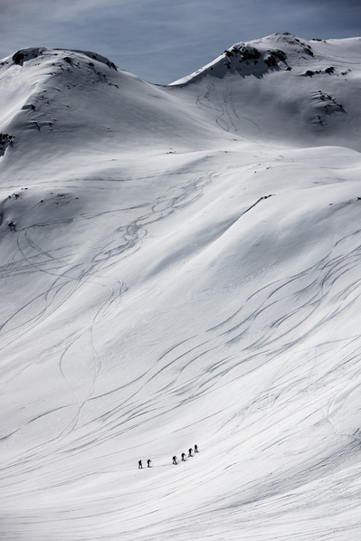A handful of explorers hike up huge snow filled mountains in the Alps. 