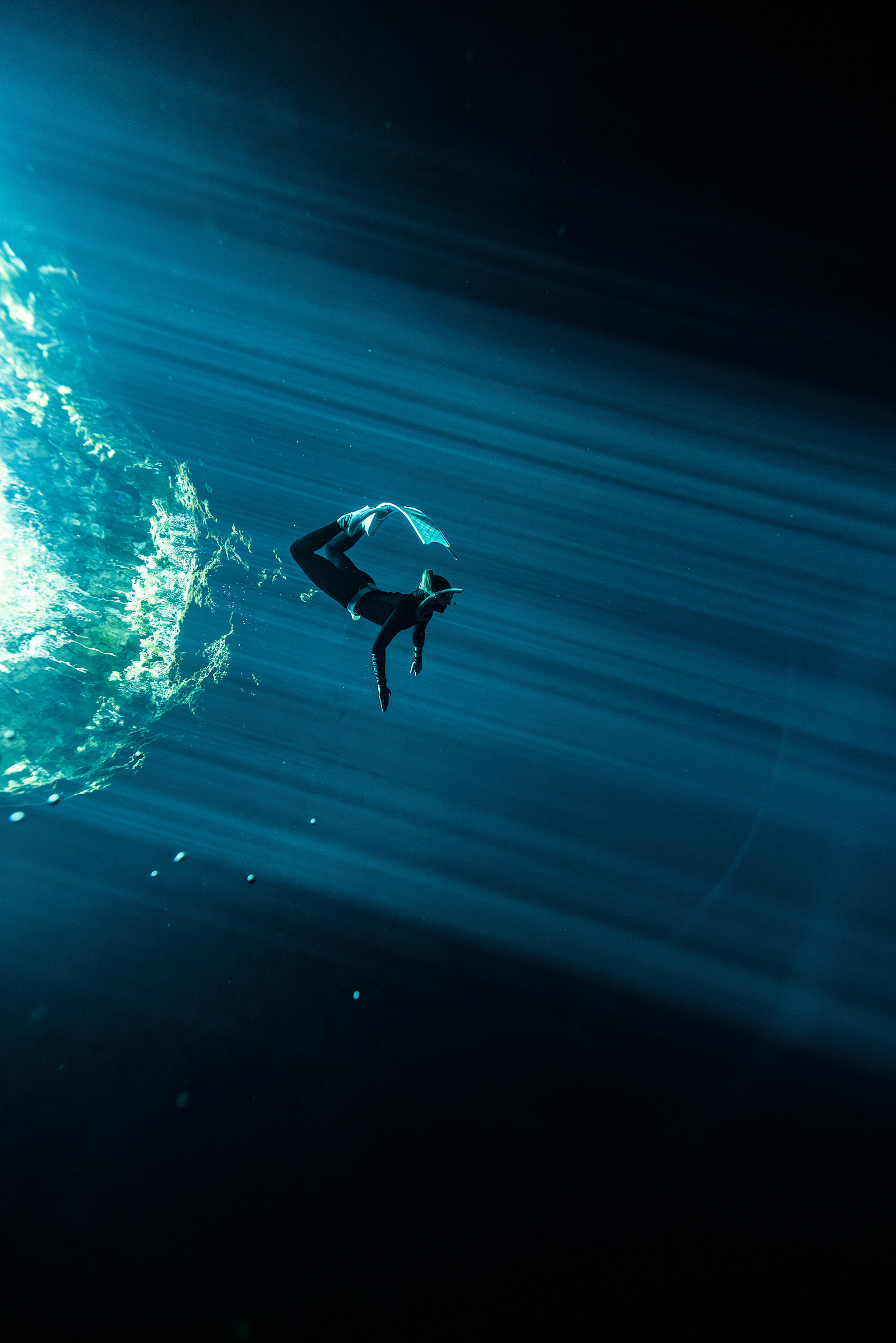 A freediver plays in a light beam underwater in a cenote in Mexico