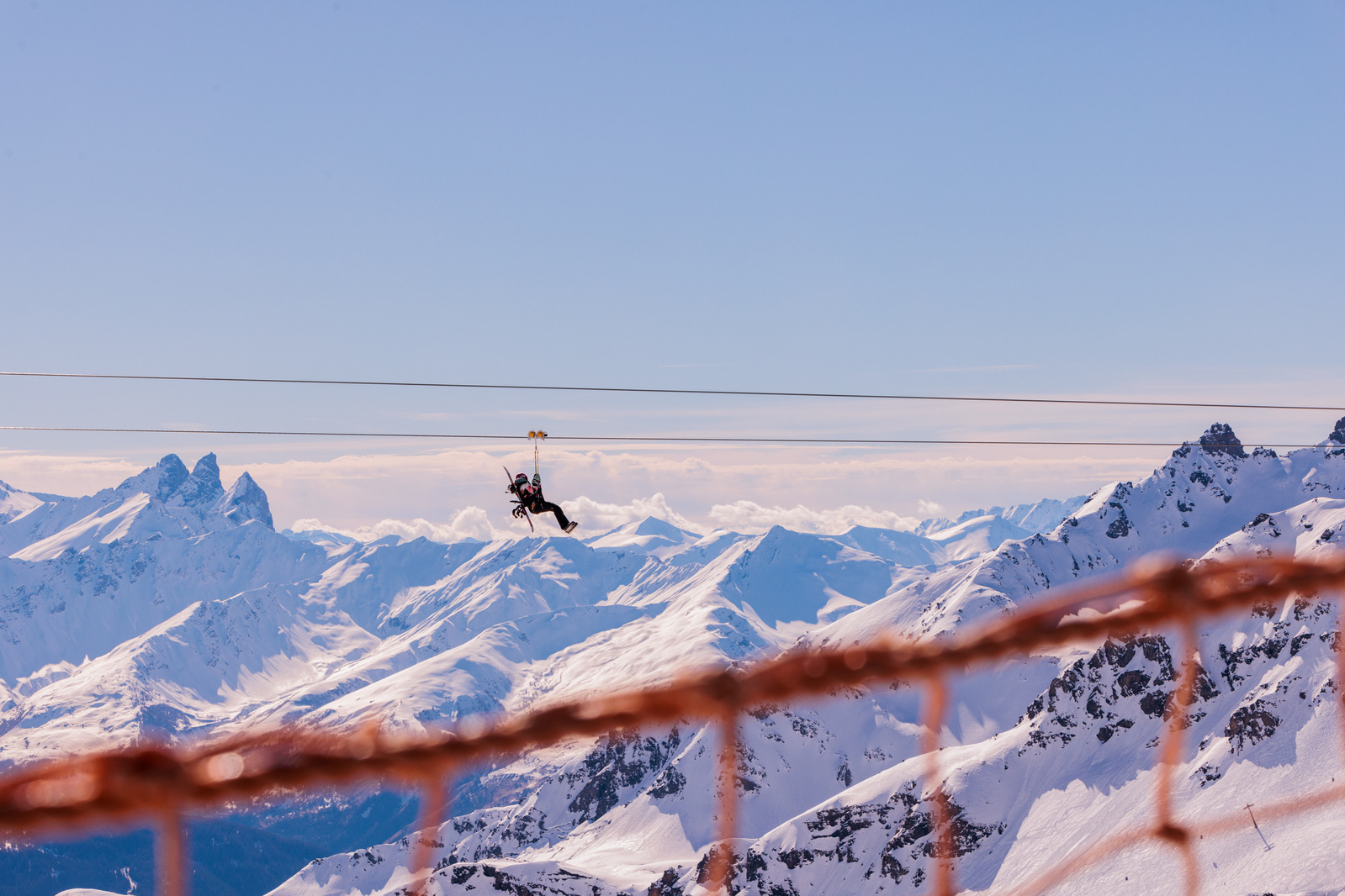 A person ziplines across a snowy mountain scene in the Alps.