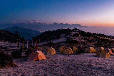 A collection of expedition tents at sunset with a snowy mountain range in the background 