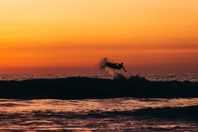 A surfer flies above the horizon line at sunset 