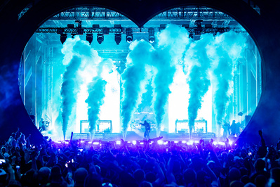 Huge jets of white smoke fill a heart shaped stage with thousands of onlookers