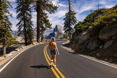 A woman walks down an iconic road in Yosemite National Park with Half Dome in the background