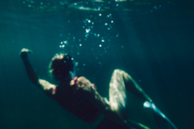 A woman sinks underwater as light highlights her features 