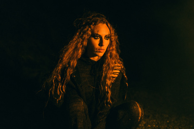 Portrait of a woman lit with the orange of a fire looking intensely off frame.  