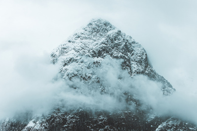 A triangular snowcapped mountain top shrouded in cloud. 