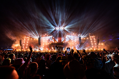 Bright lights from a huge stage with hands in the air for the closing moments of a festival