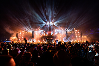 Bright lights from a huge stage with hands in the air for the closing moments of a festival