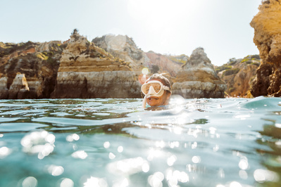 A diver smiles on the surface of the water with golden cliffs surrounding the water 
